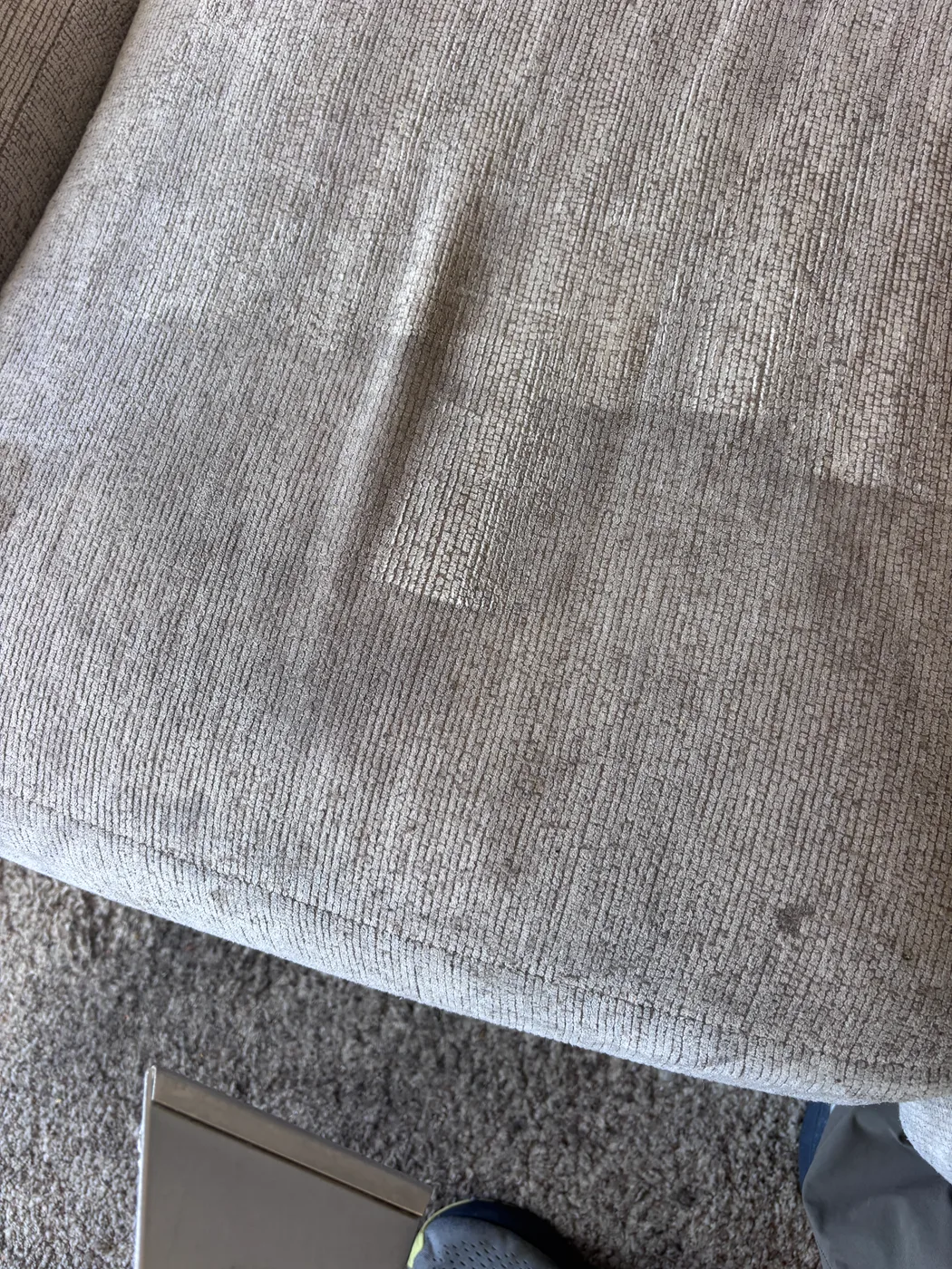 Gray upholstered cushion half cleaned, showing clean fabric beside soiled fabric