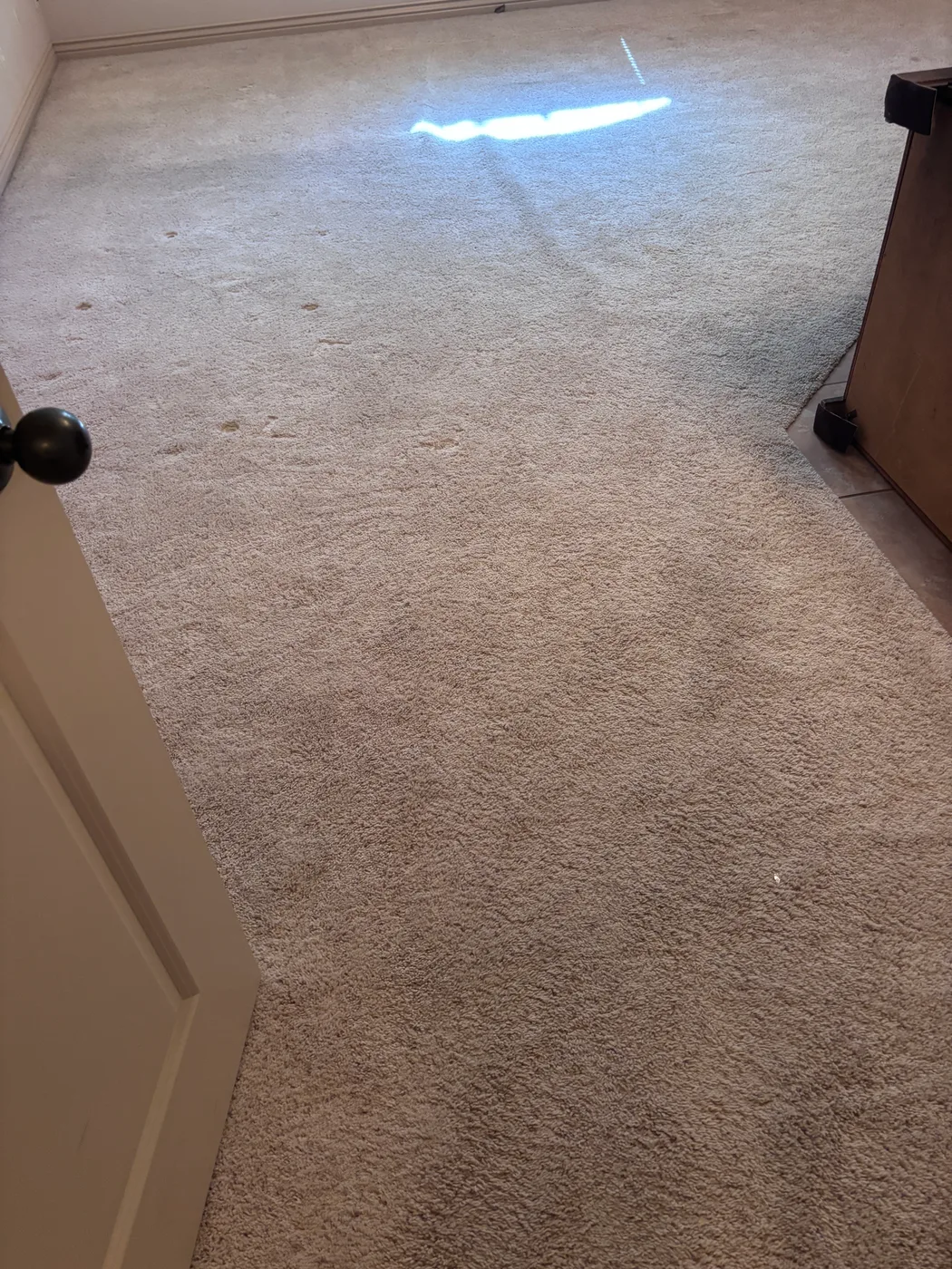 Rippled beige bedroom carpet lit by a flashlight before restretching